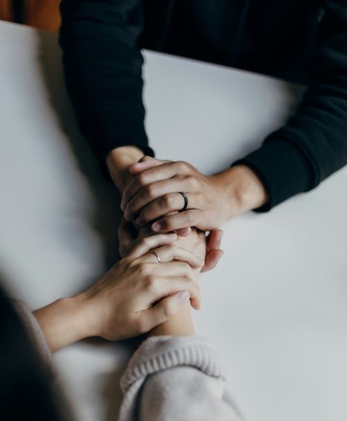 Two people clasping each other’s hands across a table in a gesture of support and comfort.